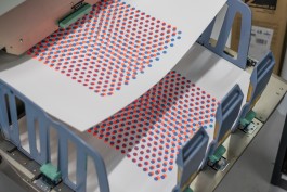 Sheets of Production Methods emerge from a risograph printer, showcasing the early stage of the artwork’s creation. The cyan and fluorescent orange halftone dots form warped grids, highlighting the imperfect registration and charming misalignments inherent to the risograph process. This image directly reflects the curatorial focus: contrasting analogue irregularities with the layered, calculated precision later introduced through screenprinting, reinforcing the dialogue between materiality and digital refinement.