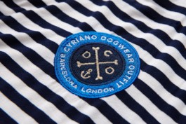 Cyriano Dogwear Outfit embroidery closeup. Blue round embroidery seal of marine inspiration. Inside theres is a cross made with two bones and an anchor. On the outside, there is written Cyriano Dogwear Outfit Barcelona London. Branding & Identity