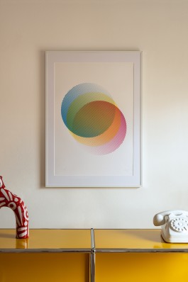 Interdisciplinarity framed. Framed artwork Interdisciplinarity by Marçal Prats displayed in a clean, modern interior. The print features three overlapping linear circles in cyan, magenta, and yellow, forming a Venn diagram of blended colours. Mounted above a glossy yellow cabinet with a red sculptural object and a porcelain sculpture of vintage white rotary phone, the display highlights the print’s conceptual focus on convergence and visual harmony.